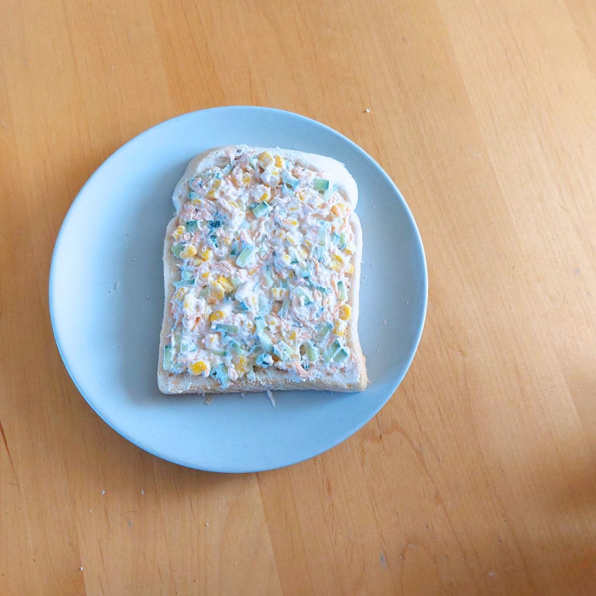 white bread slice topped with vegetable cheese spread placed on grey plate on wooden table.