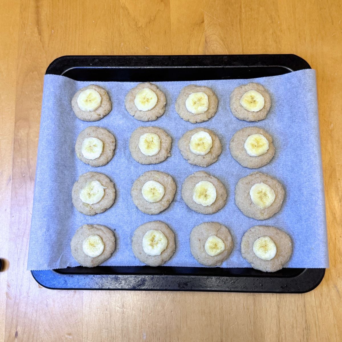 almond banana cookies topped with banana slice arranged on lined baking sheet.