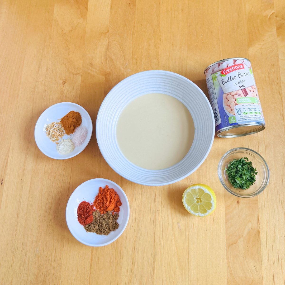 tahini, spices and canned butter beans on wooden table.