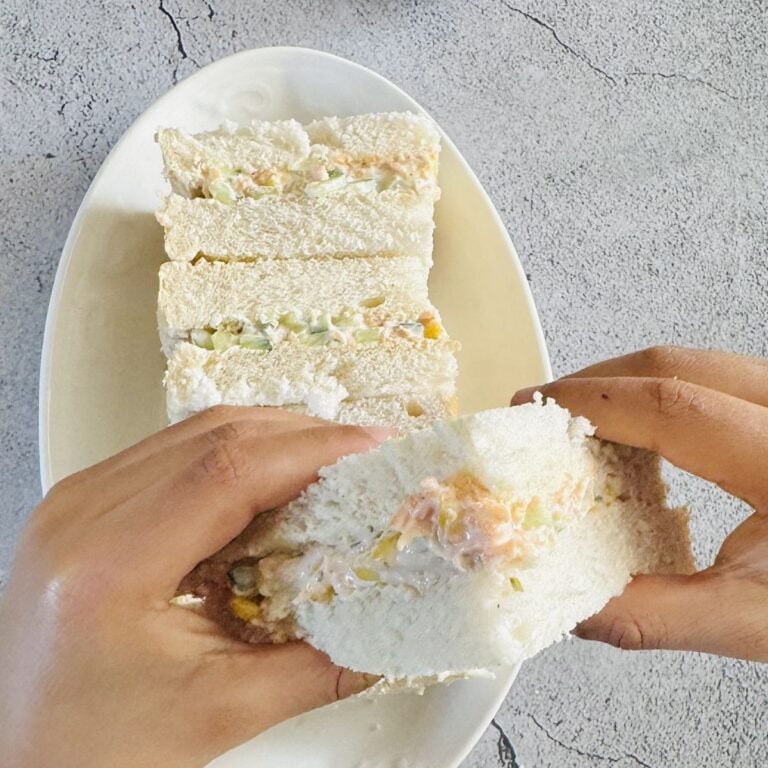 child holding sandwich with two hands on top of white plate of sandwiches