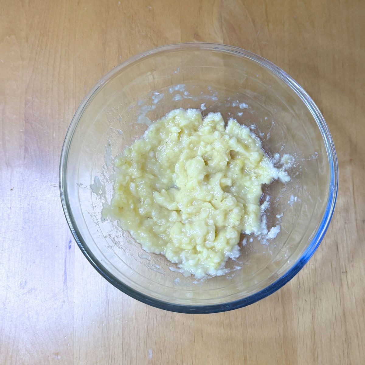 glass bowl of mashed banana placed on wooden table.