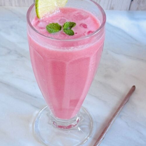 glass of watermelon coconut milk cooler placed on marble along with a eco friendly coconut leaf straw.