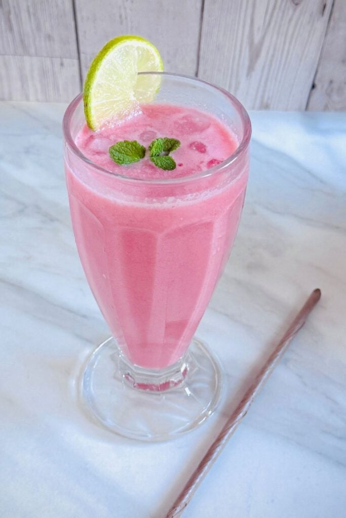 glass of watermelon coconut milk cooler placed on marble along with a eco friendly coconut leaf straw.