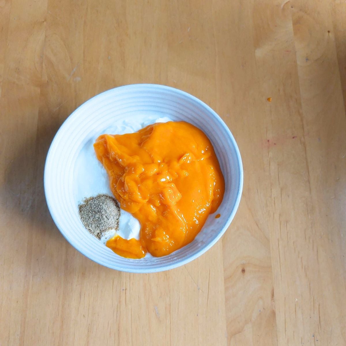 white bowl of yogurt, mango puree and cardamom powder placed on wooden table.