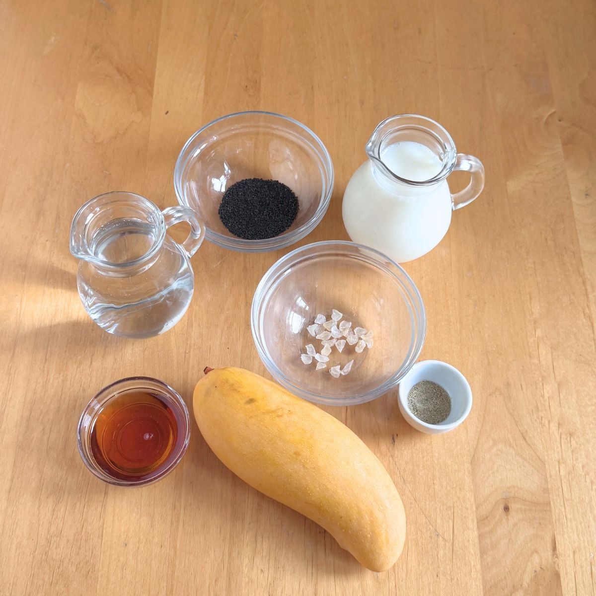 Ingredients to make mango gond katira sabja drink placed on wooden table.