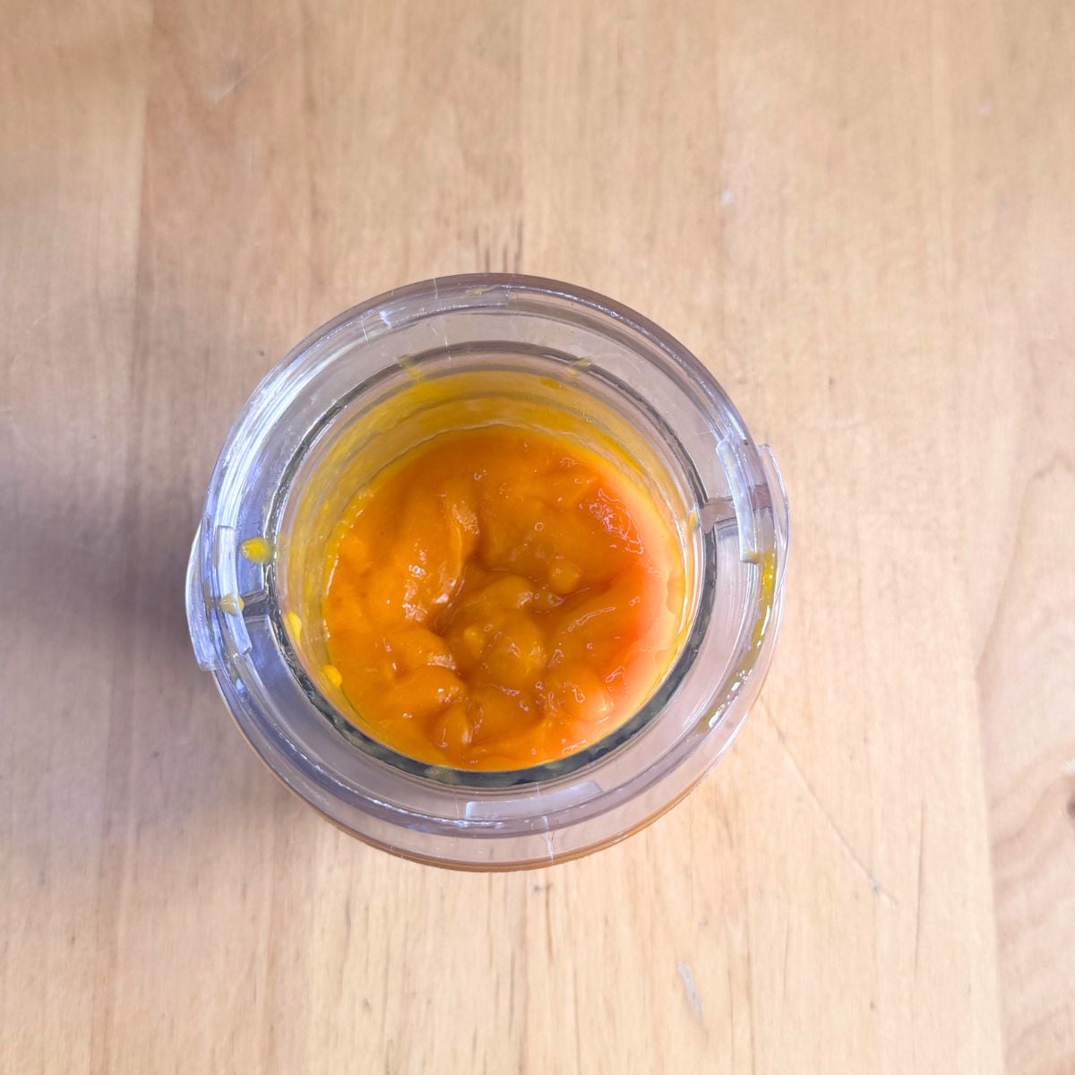 blender jar with pureed mango placed on wooden table.