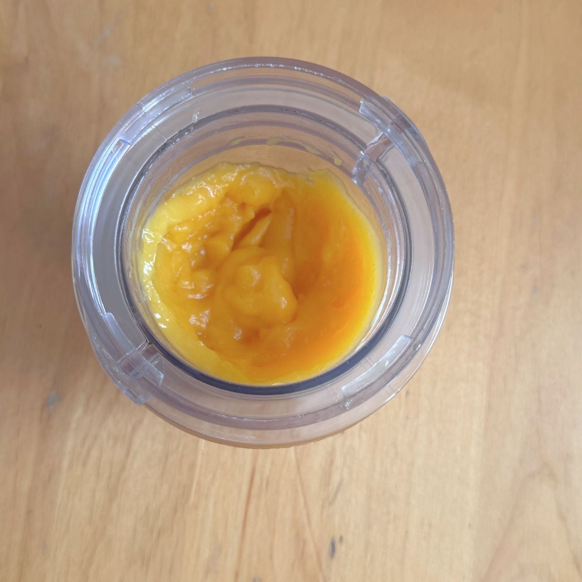 blender jar with pureed mango placed on wooden table.