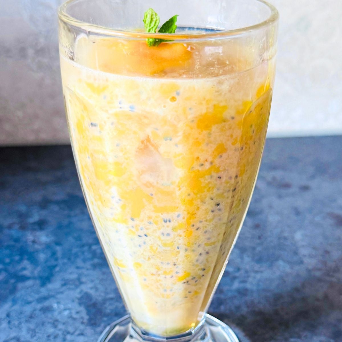 front view of a glass of mango drink with basil seeds and gond katira placed on a platform.