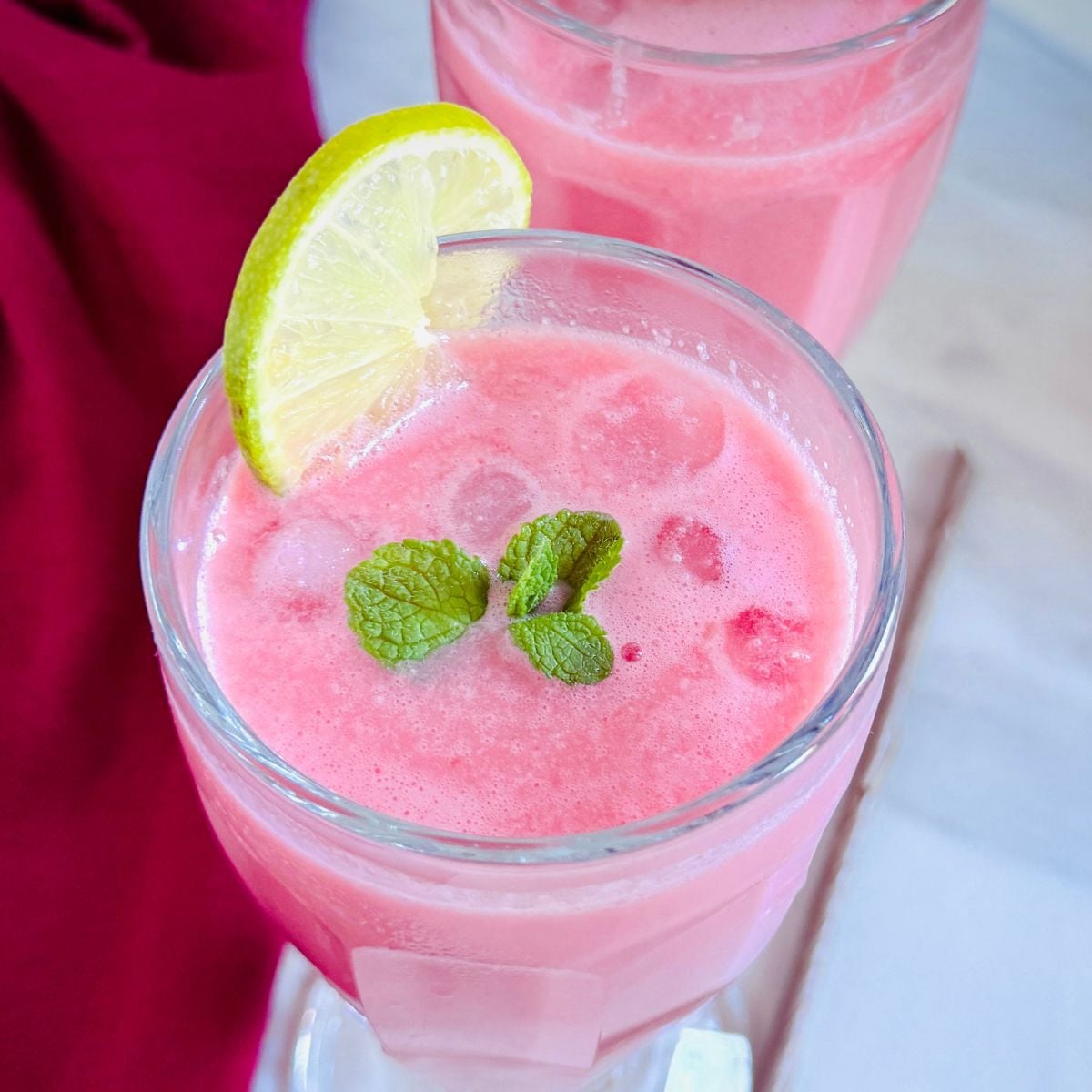 top view of glass of pink watermelon coconut milk drink garnished with mint and lemon slice.