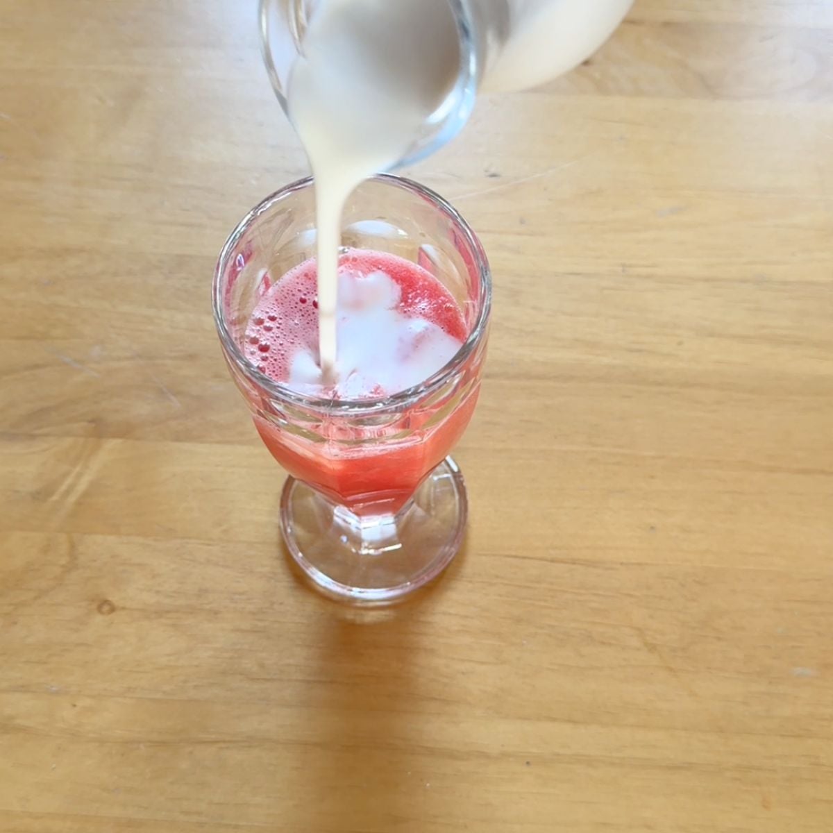 pouring coconut milk into a glass of watermelon juice.