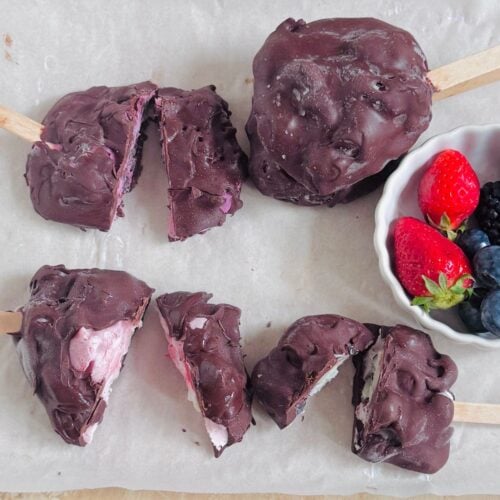 chocolate covered frozen yogurt berry pops on baking sheet along with a bowl of berries.