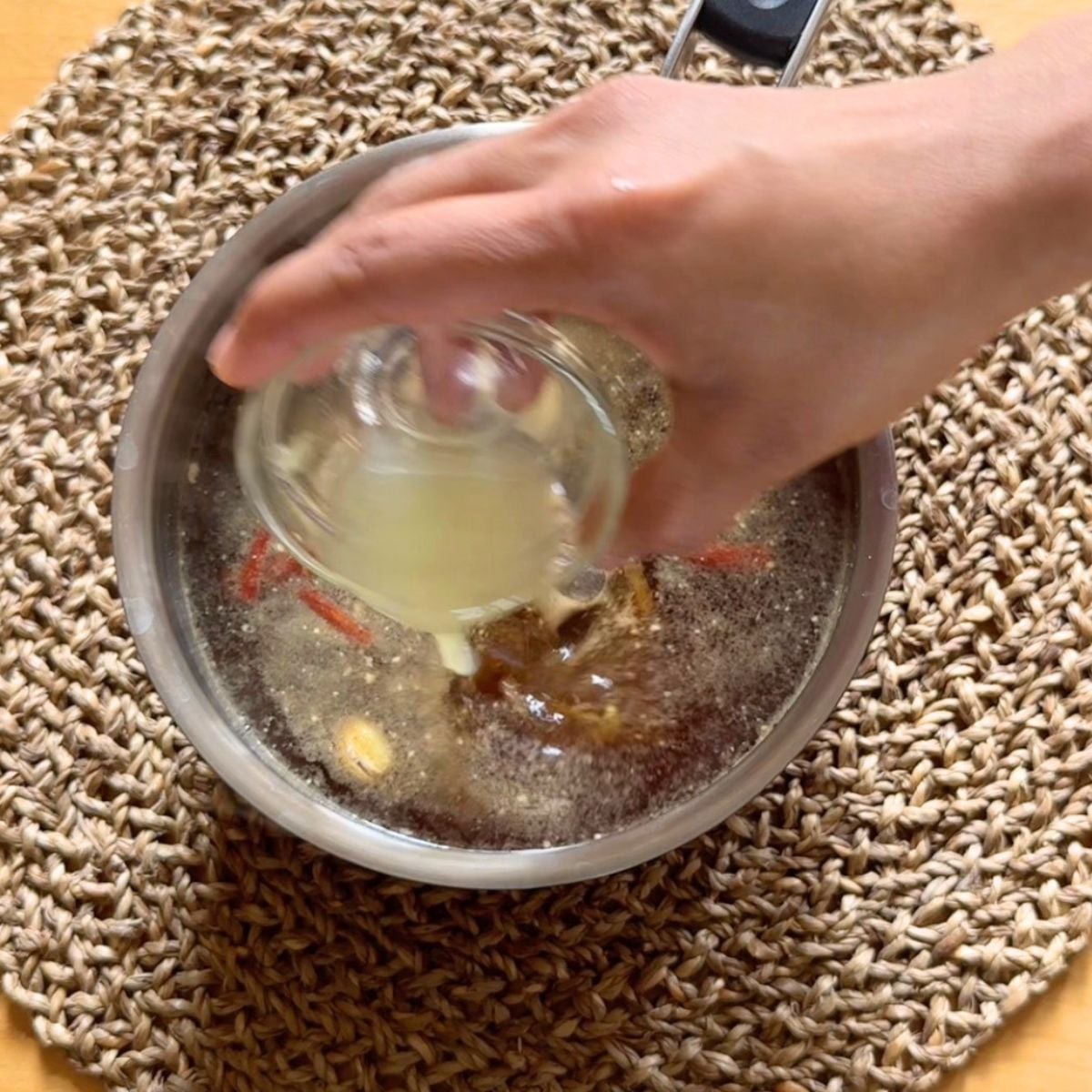 pouring lemon juice into a steel pot of brewed lemon ginger tea.