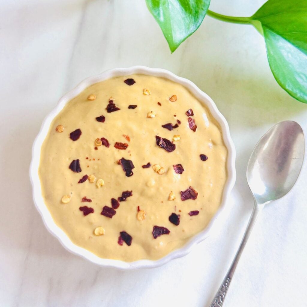 top view of white bowl of mango chilli peanut butter dipping sauce placed on marble along with a spoon.