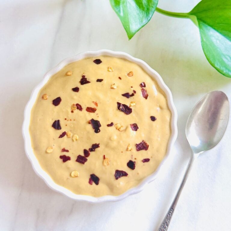 top view of white bowl of mango chilli peanut butter dipping sauce placed on marble along with a spoon.