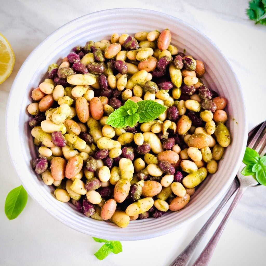 close up view of bowl of dense bean salad placed on marble along with cutlery.