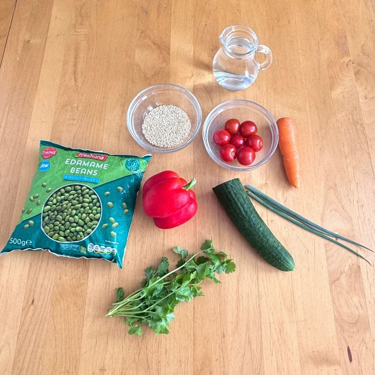 vegetables, quinoa, edamame and water on wooden table.