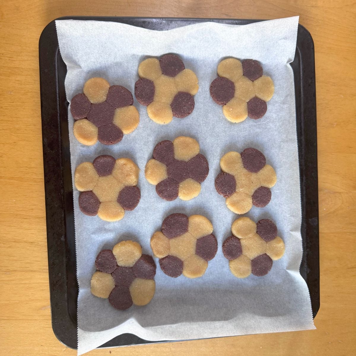 two toned flower cookies on lined baking sheet placed on wooden table.