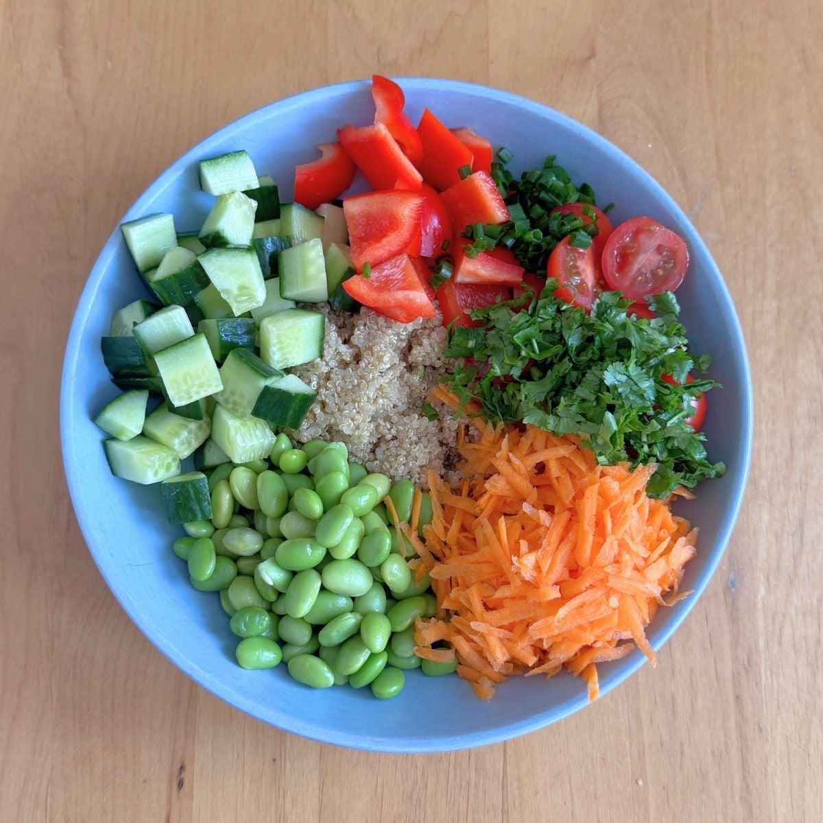 blue bowl filled with quinoa, vegetables and edamame placed on wooden table.