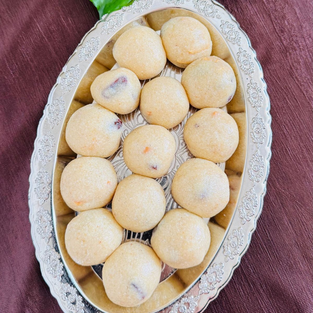oval silver plate arranged with rava laddus placed on brown cloth.