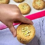 a child holding 3 ingredient almond flour pistachio cookie from a stack of them.