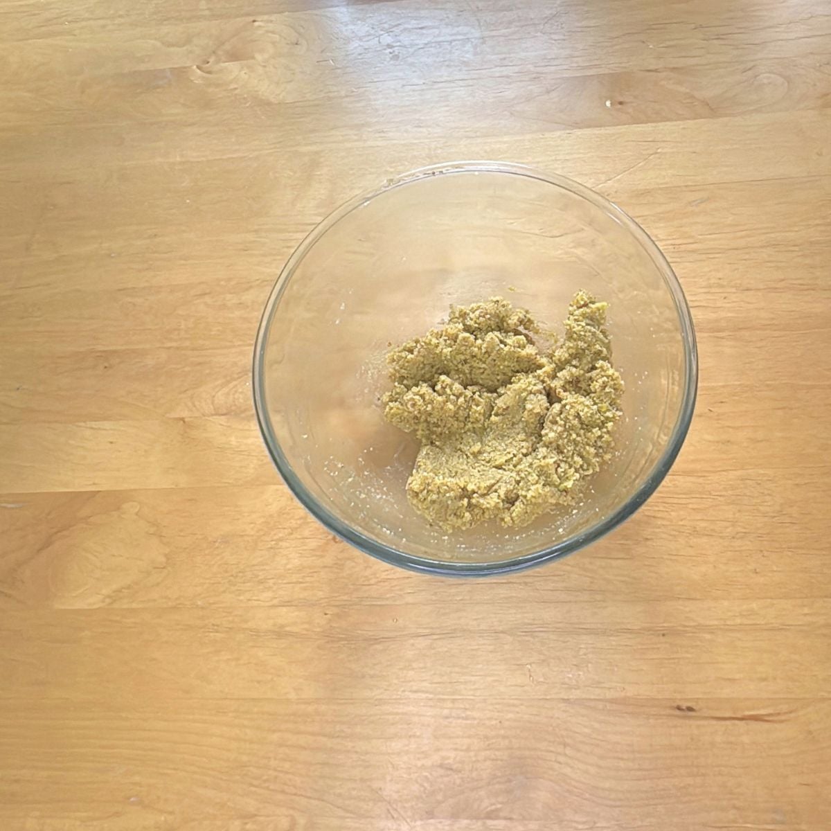 glass bowl of almond pistachio dough on wooden table.
