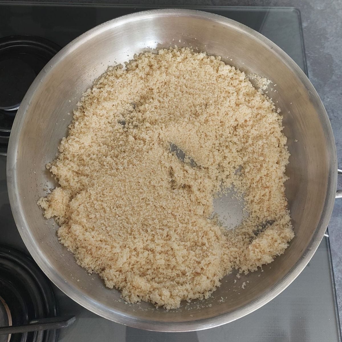 roasting semolina in a wide steel pan on black stovetop.