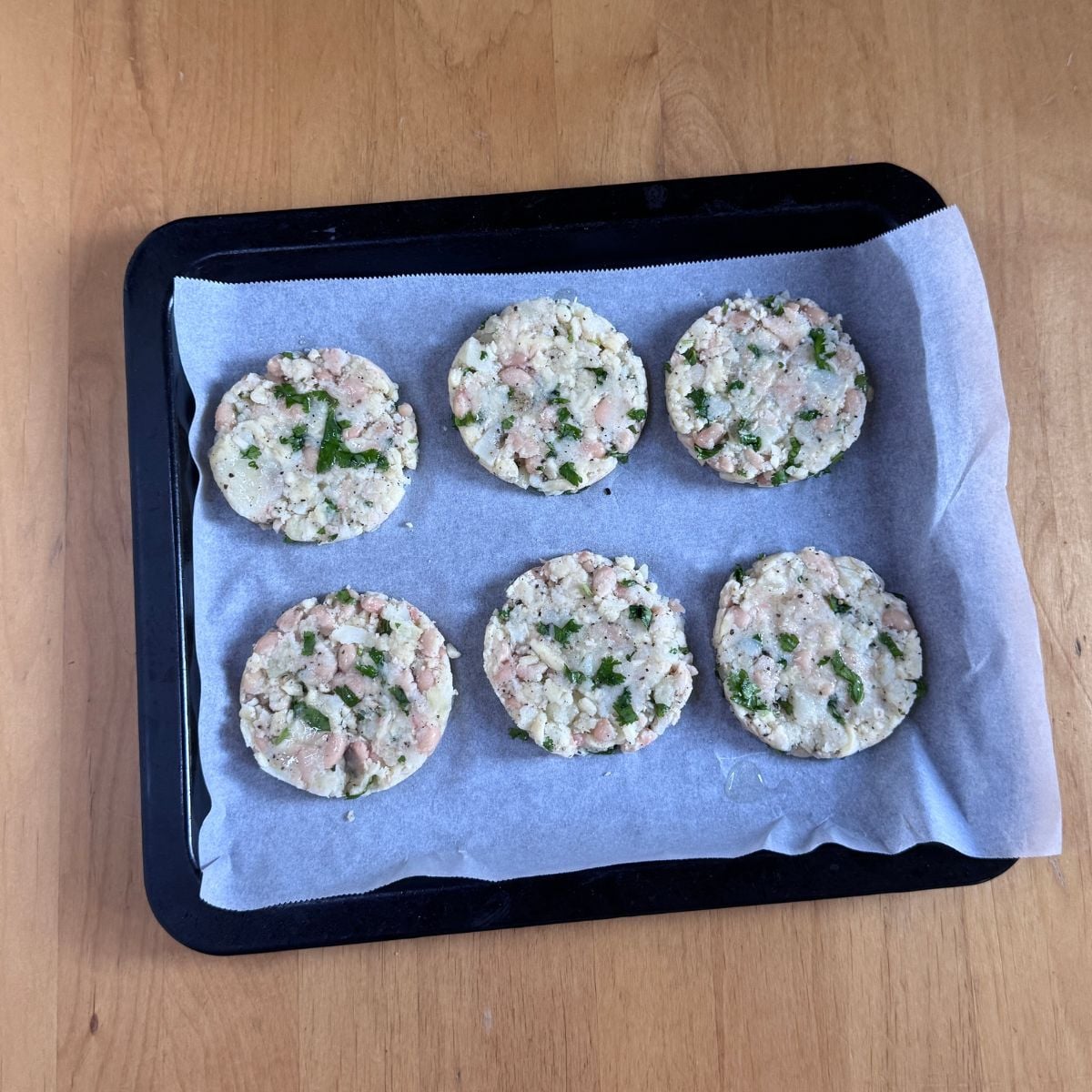 bean potato patties on lined baking tray placed on wooden table.