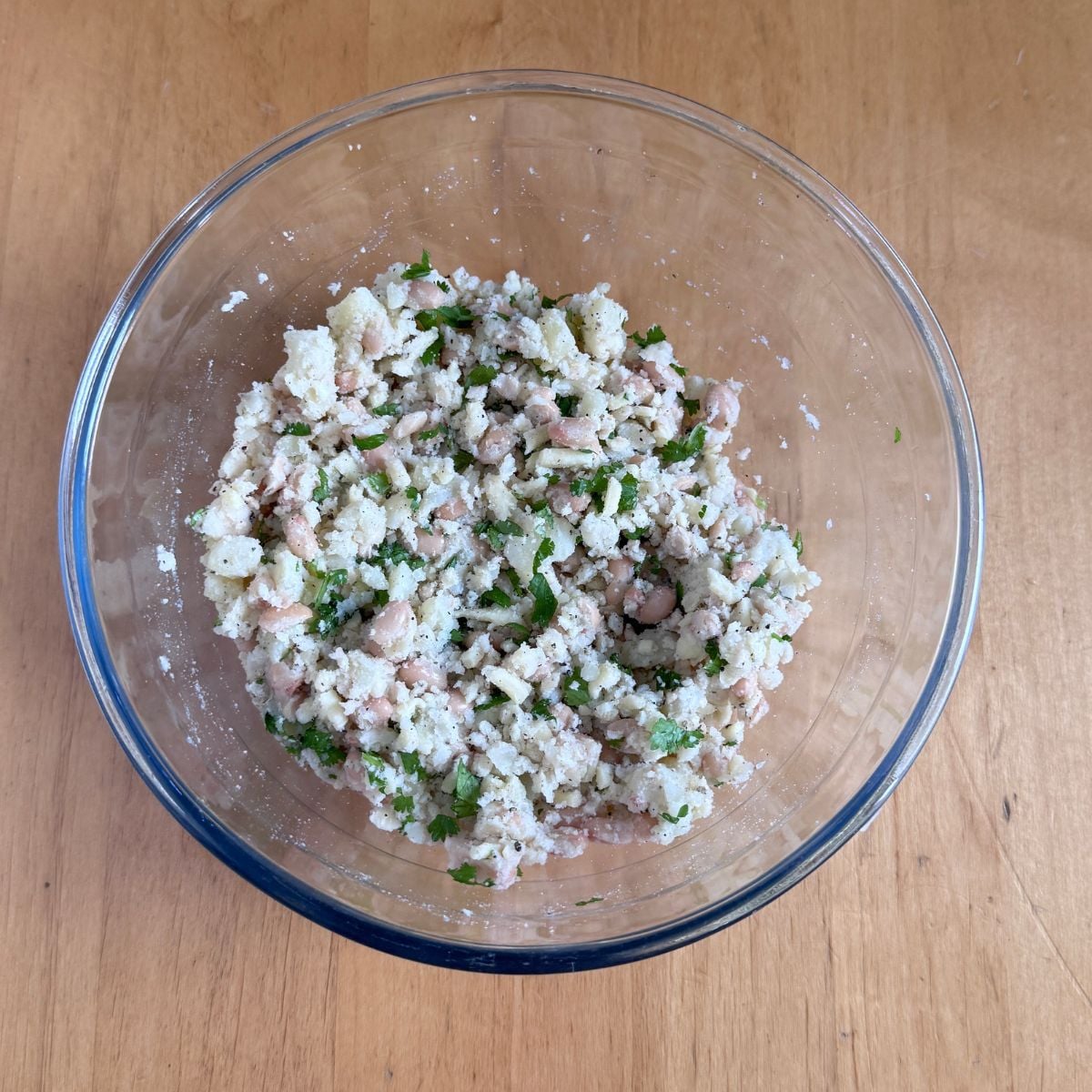 glass bowl of white bean potato cheese patties mixture placed on wooden table.