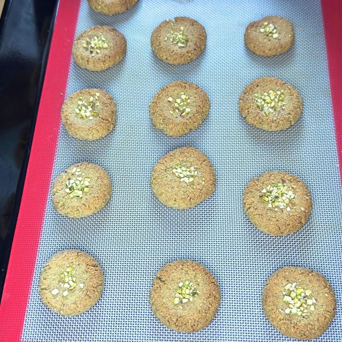 baked gluten free almond flour pistachio cookies arranged on lined baking tray.