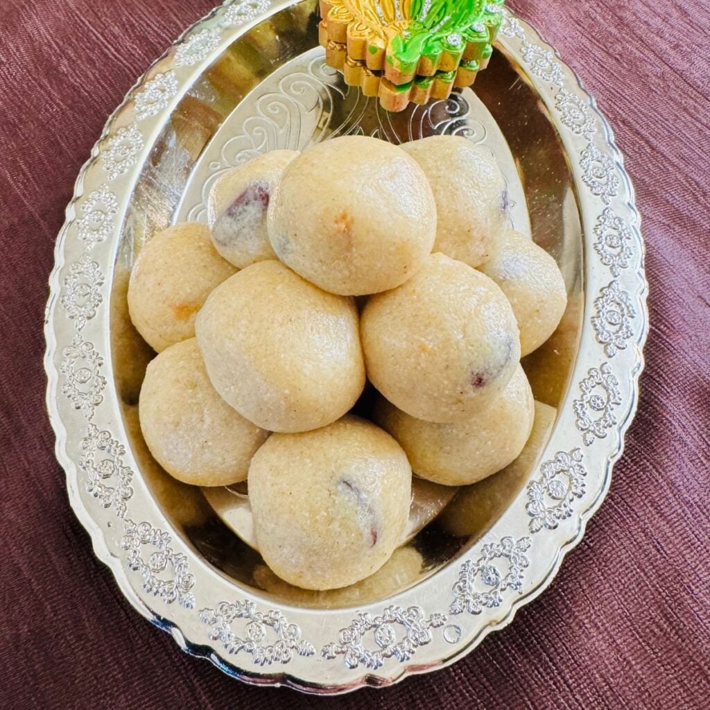 rava laddu with condensed milk arranged on a silver plate placed on brown cloth.