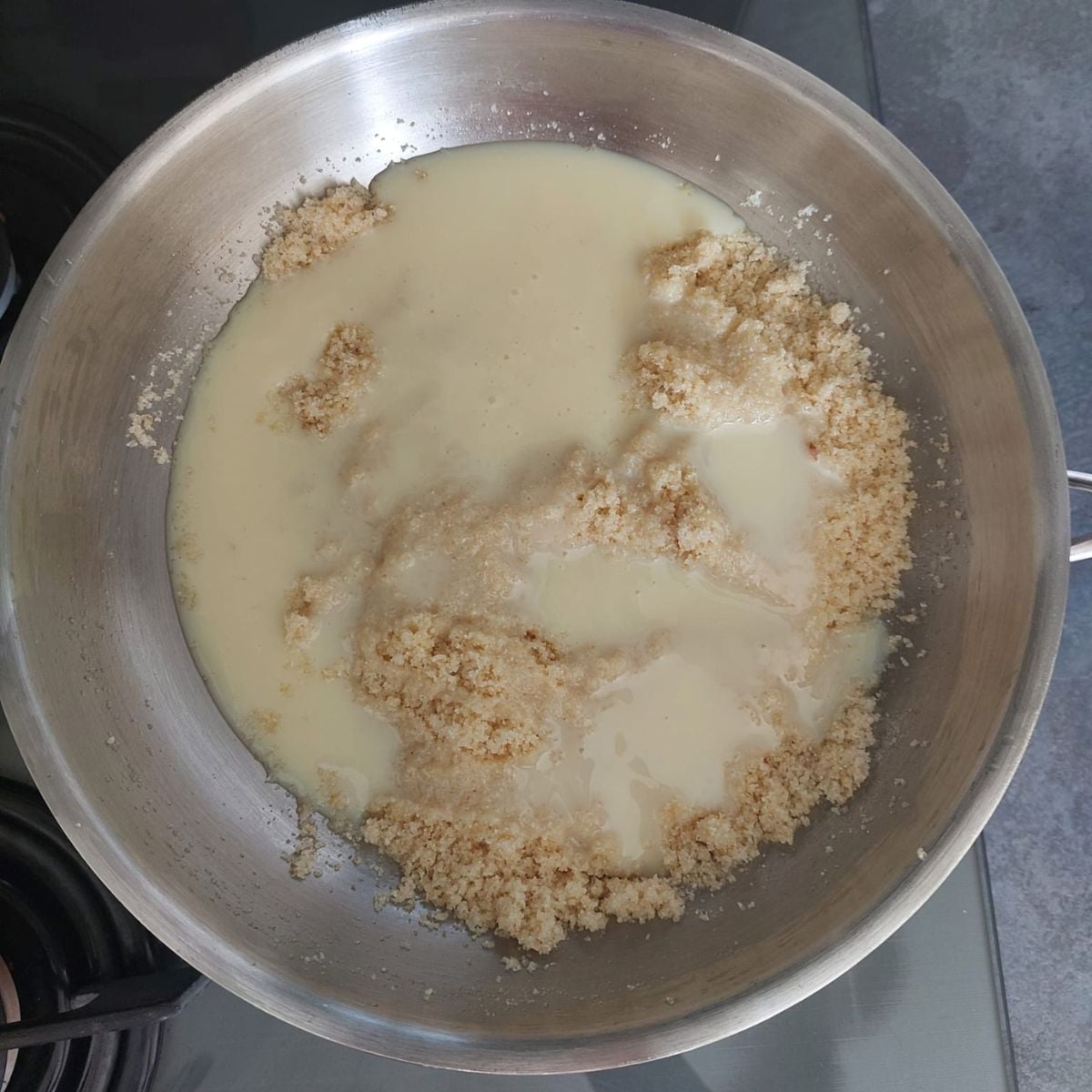 steel pan with semolina and condensed milk placed on black stovetop.