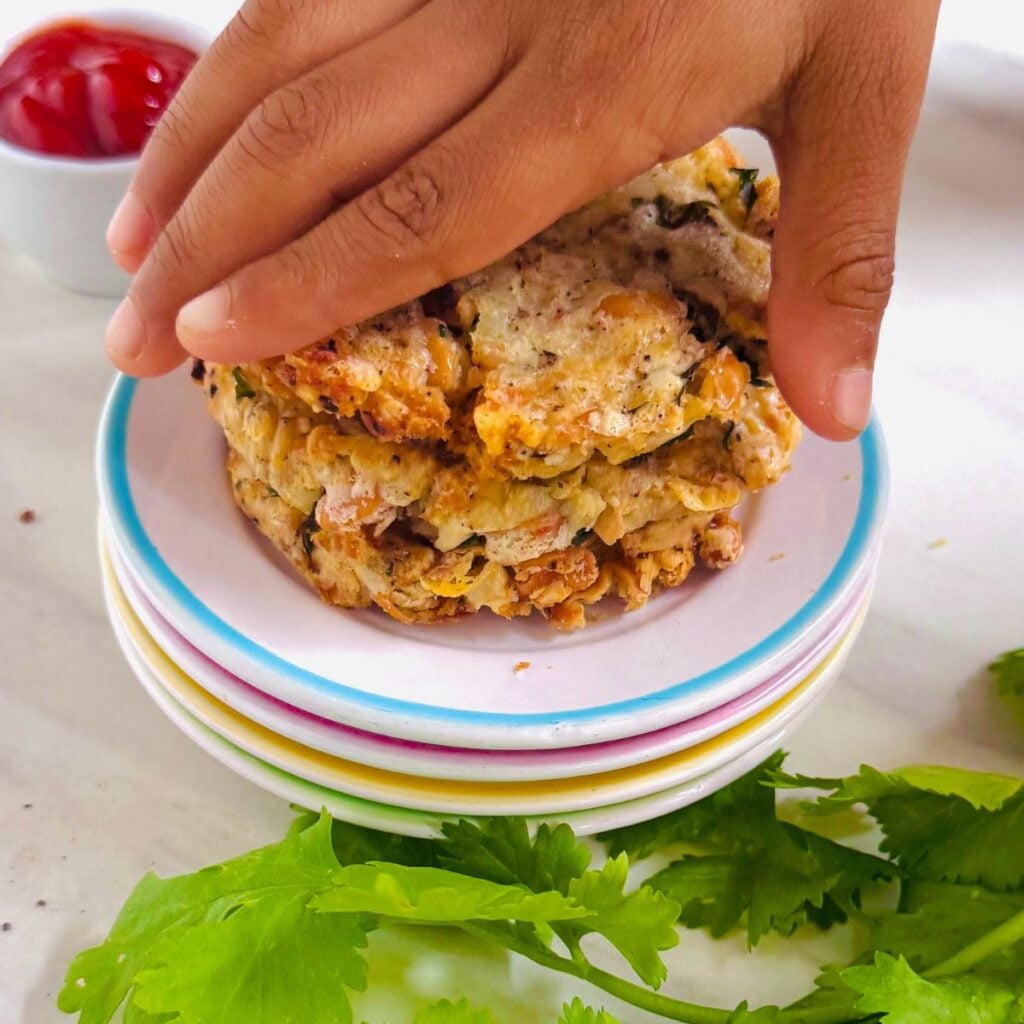 child picking baked bean potato cheese patties from a stack on white plate.