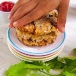 child picking baked bean potato cheese patties from a stack on white plate.