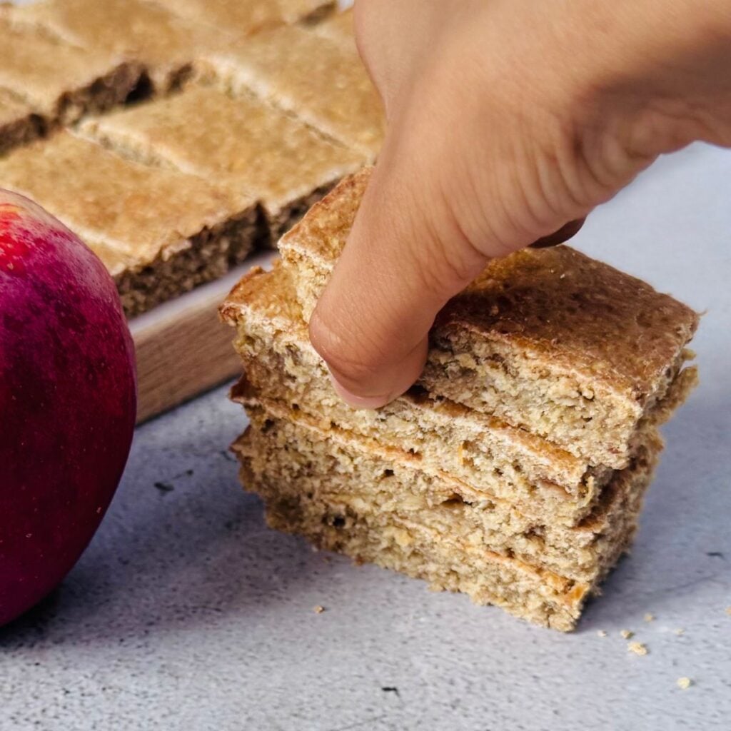 child picking apple oat bars from stack placed on granite.