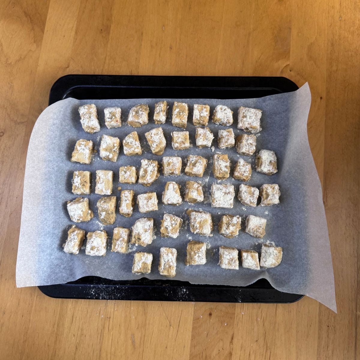 gram flour double coated tofu arranged on lined baking tray placed on wooden table.