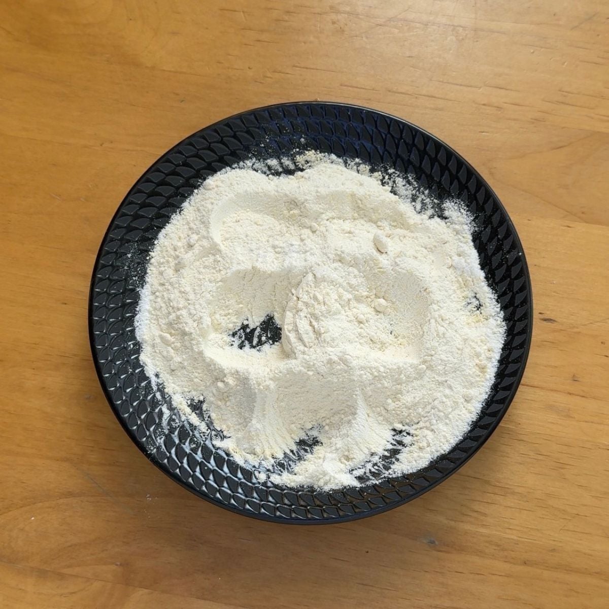 black plate of flour on wooden table.