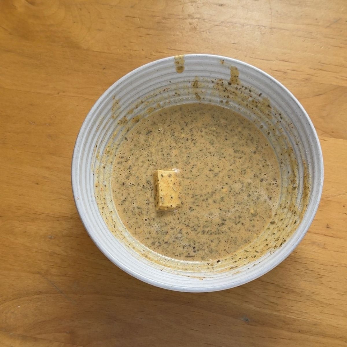 white bowl of spiced gram flour batter with a piece of tofu in it.