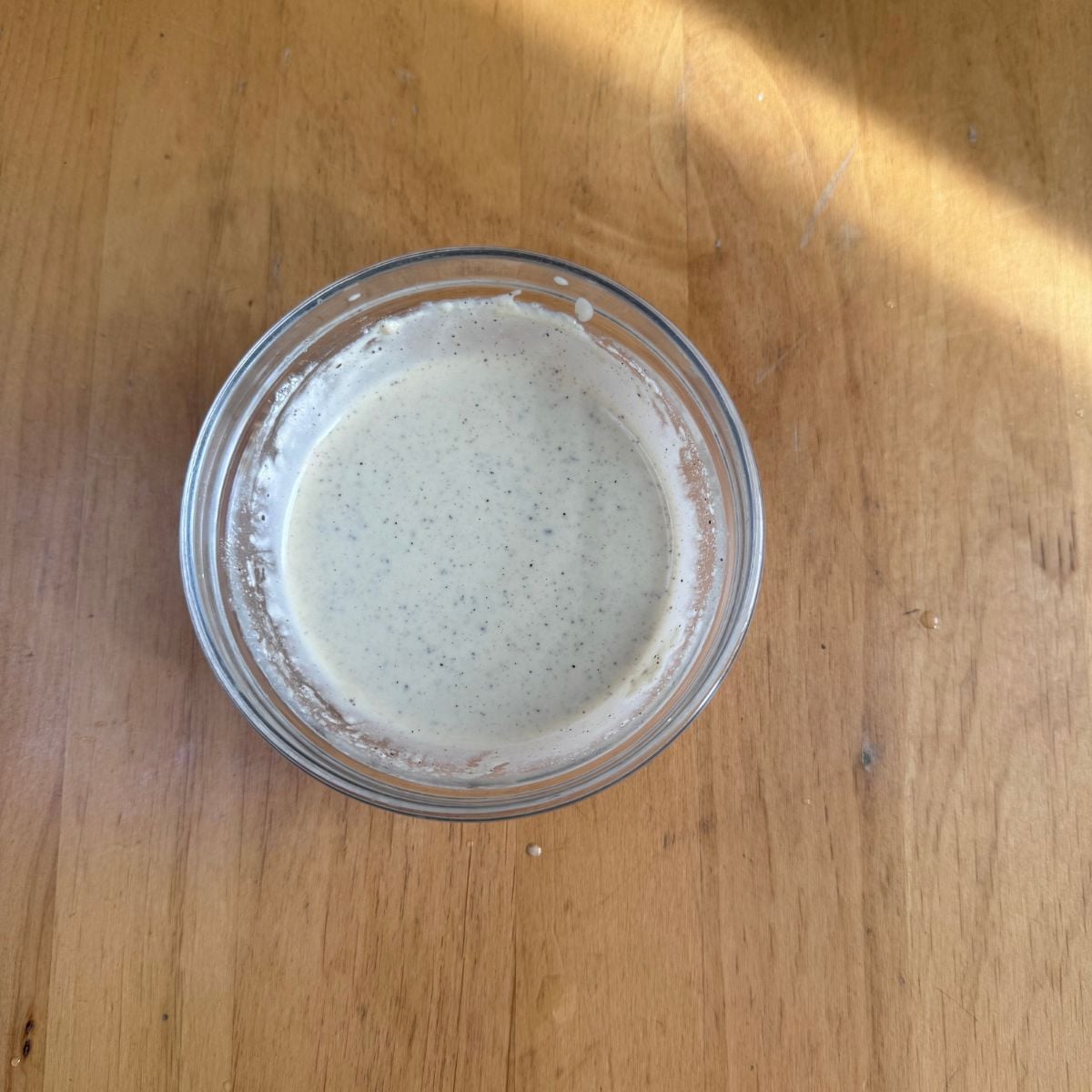 glass bowl of tahini lemon dressing placed on wooden table.